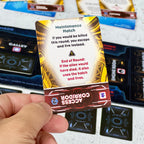 Maintenance Hatch card from a board game held by a hand with game components in the background. The card reads "Maintenance Hatch": if you would be killed this round, you escape and live instead. End of round, if the alien would have died, it also uses the hatch and lives. 