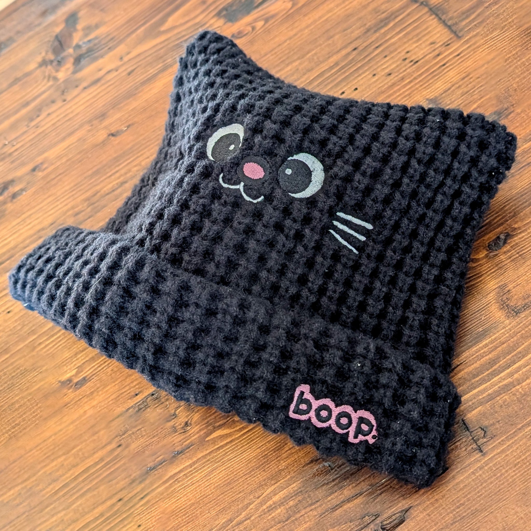 Black knitted cat-shaped beanie with a 'boop' label on a wooden surface