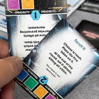 Close-up of a card with game text and priority markers held by a hand. The text reads: Torch it, choose a room, place the fire token on it. At the end of the round, set it ablaze, killing all within. The room is not destroyed. 